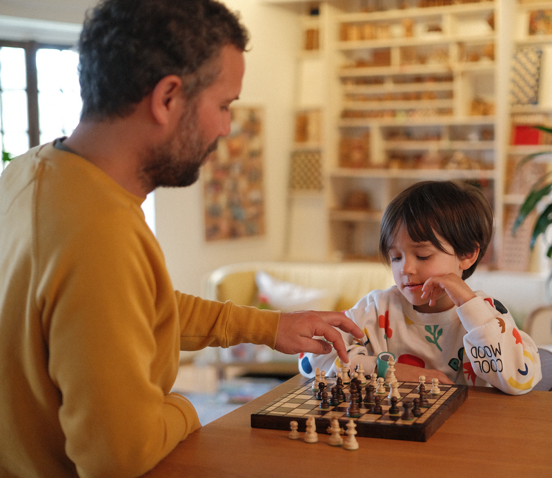 Un père et son fils jouent aux échecs en bois à la maison