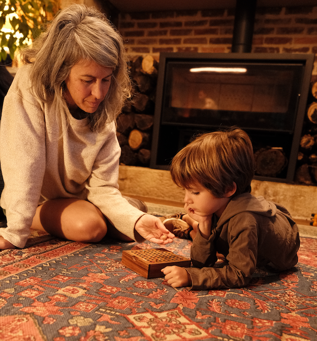 Une femme et un jeune enfant jouent avec un jeu en bois sur un tapis, devant la cheminée
