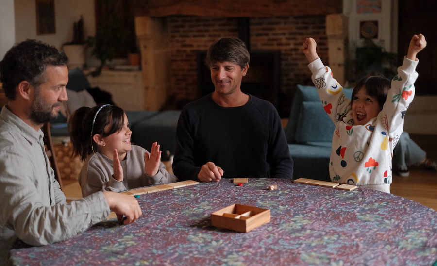 Famille autour d'une table, un enfant lève les bras en gagnant une partie de jeu en bois