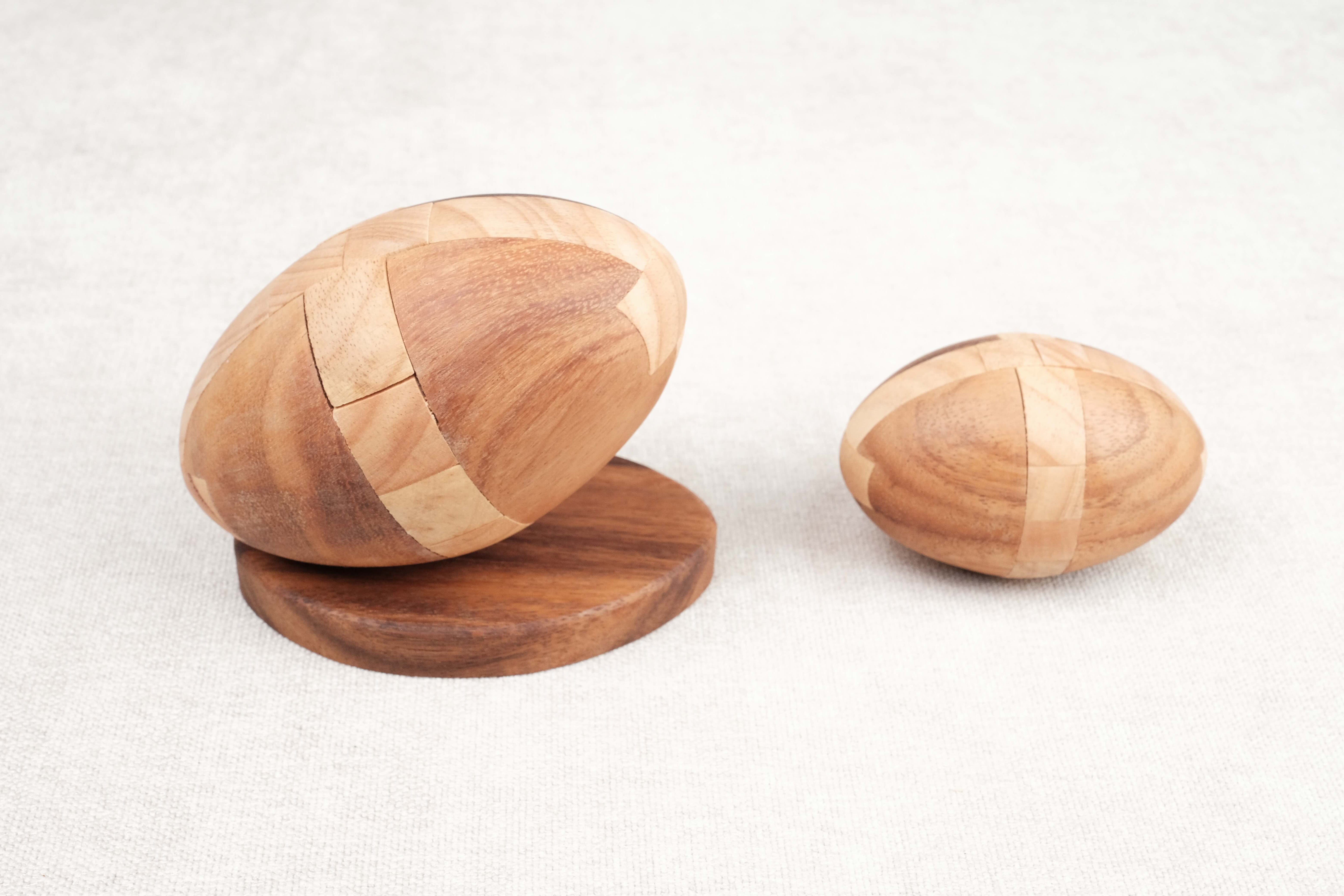 Comparatif tailles : Deux casse-têtes Ballon de Rugby en bois côte à côte, modèles M et L.