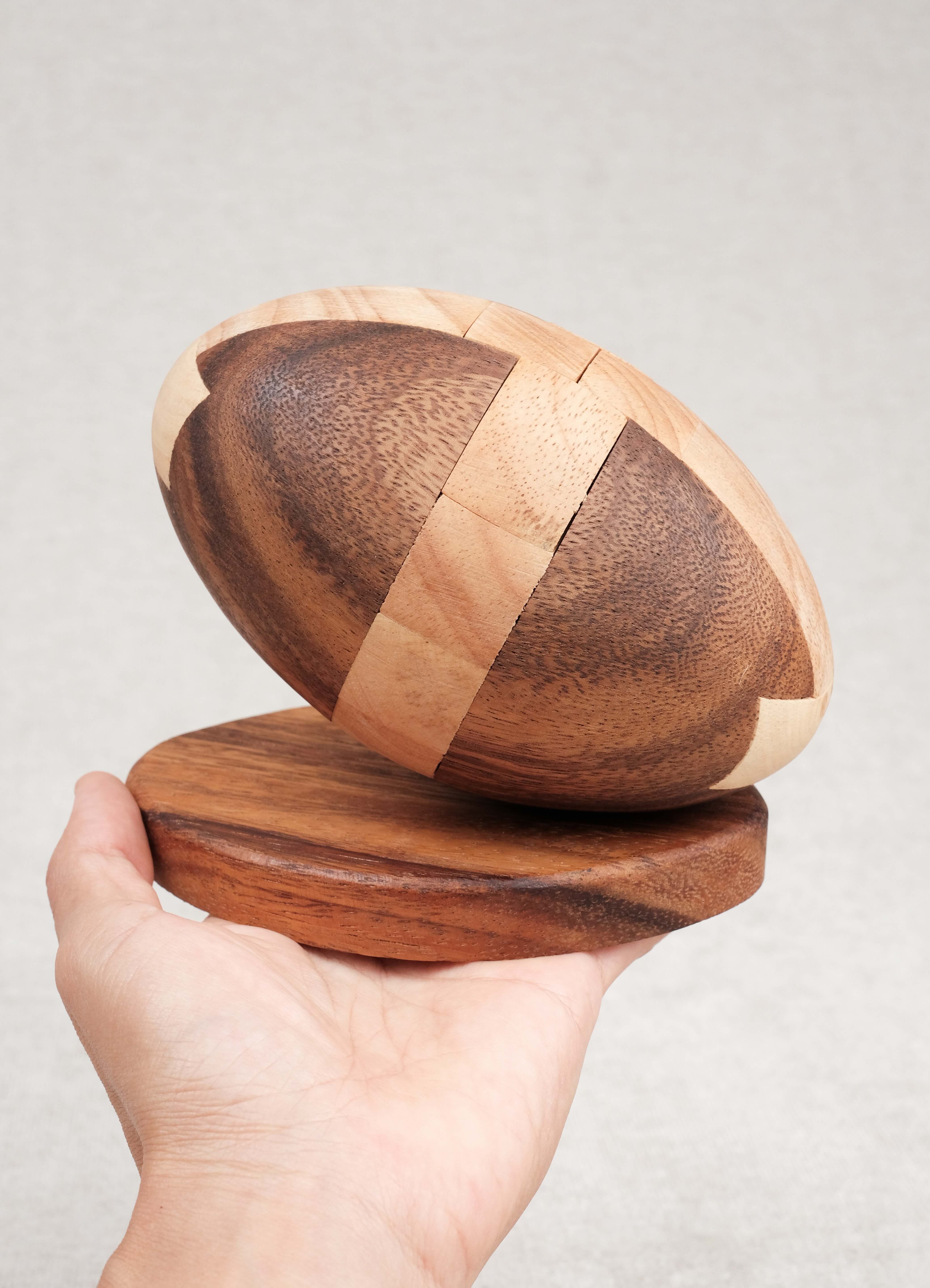 Prise en main : Ballon de Rugby en bois sur socle tenu dans une main, taille L.