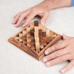 Deux mains reconstituant le casse-tête Grande Kheops en bois sur une table.