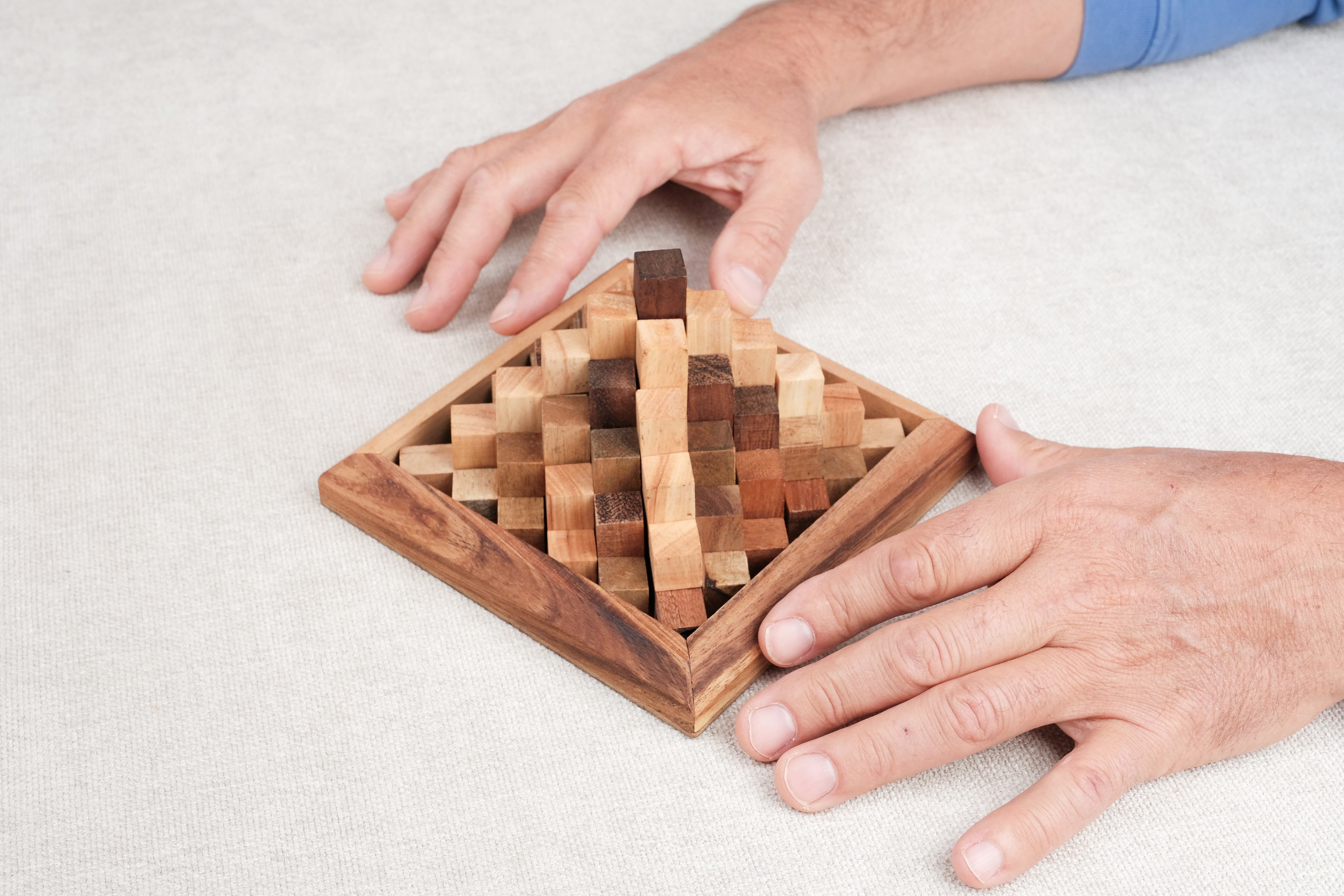 Deux mains reconstituant le casse-tête Grande Kheops en bois sur une table.