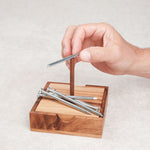 Main en train de positionner un clou sur la base en bois du casse-tête Les Clous