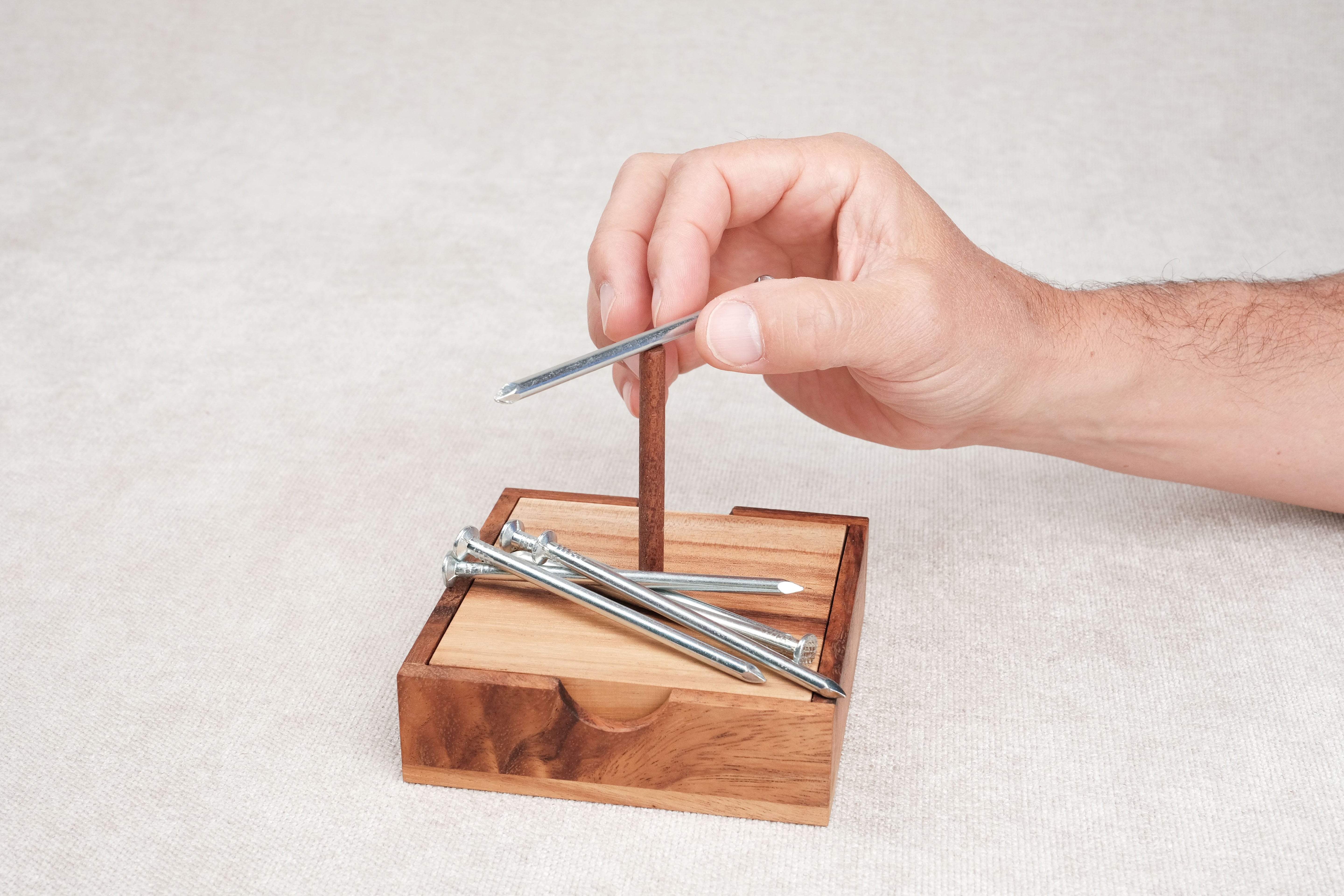 Main en train de positionner un clou sur la base en bois du casse-tête Les Clous