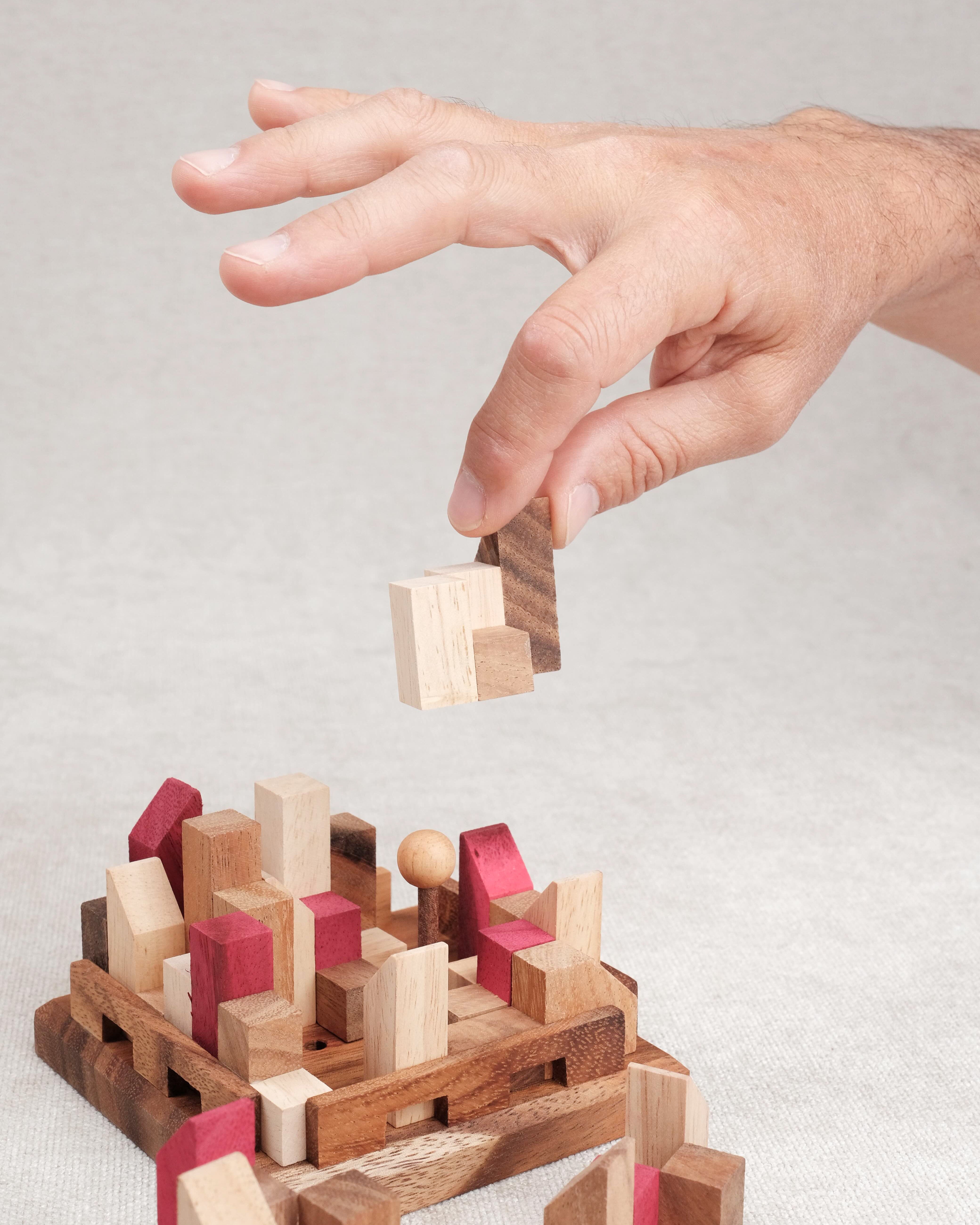 Main qui manipule une pièce du casse-tête La Cité Infernale en bois – Puzzle multi-combinaisons – Jeux Faugère