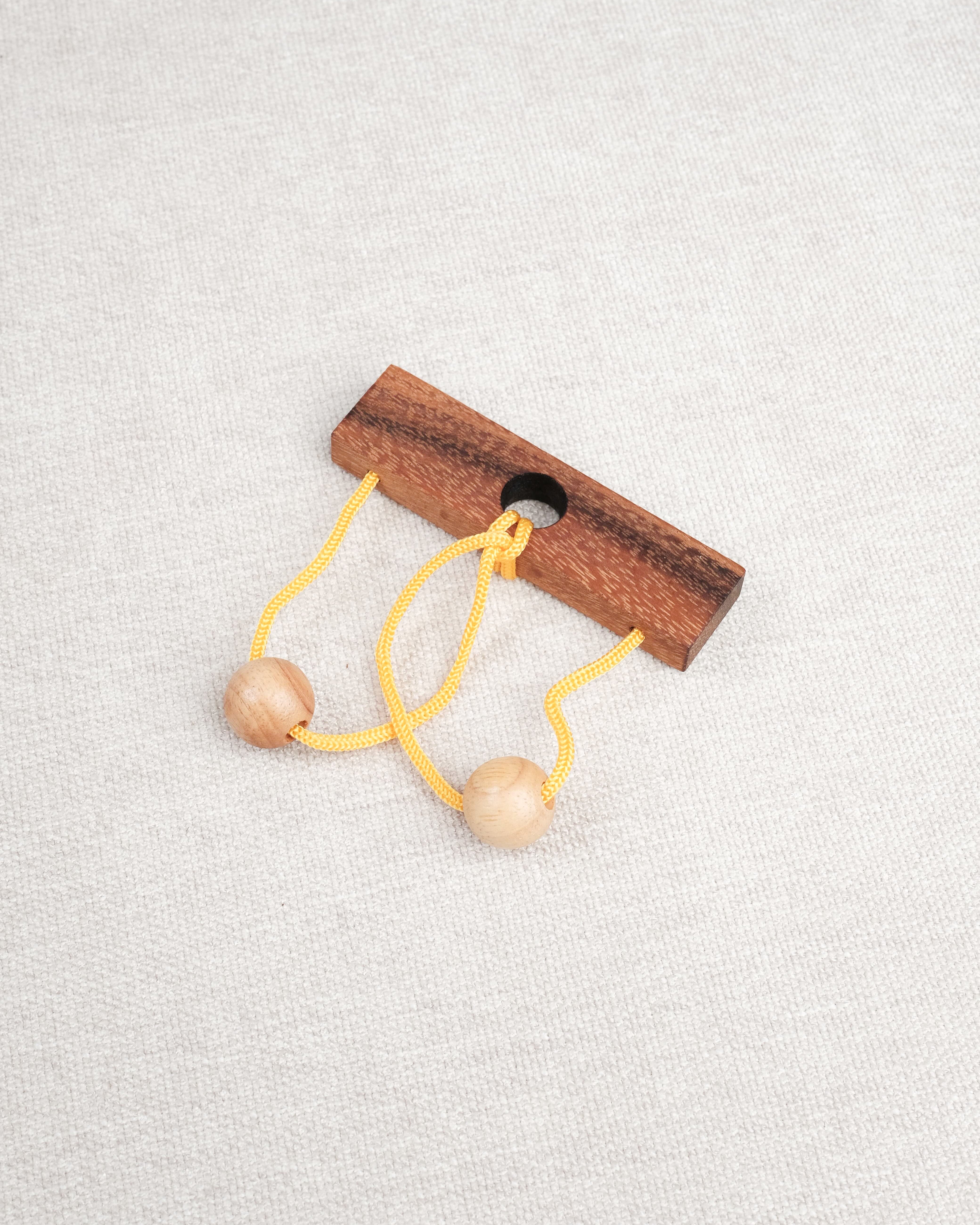 Casse-tête en bois Roméo & Juliette avec ficelle jaune et deux boules en bois.