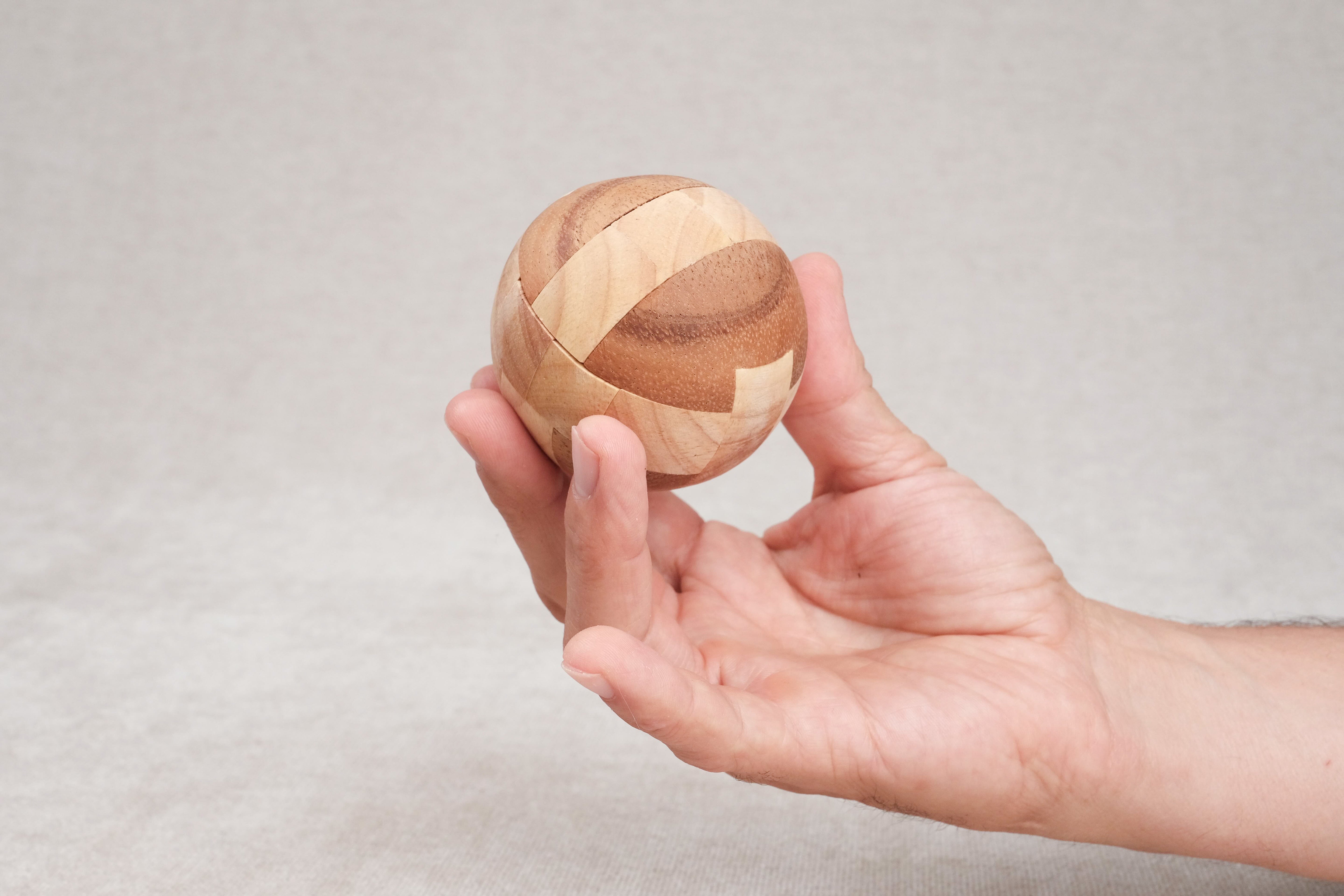 Ballon de foot en bois tenu dans une main, vue de taille compacte.