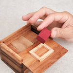 Main insérant la pièce rouge dans la boîte en bois.