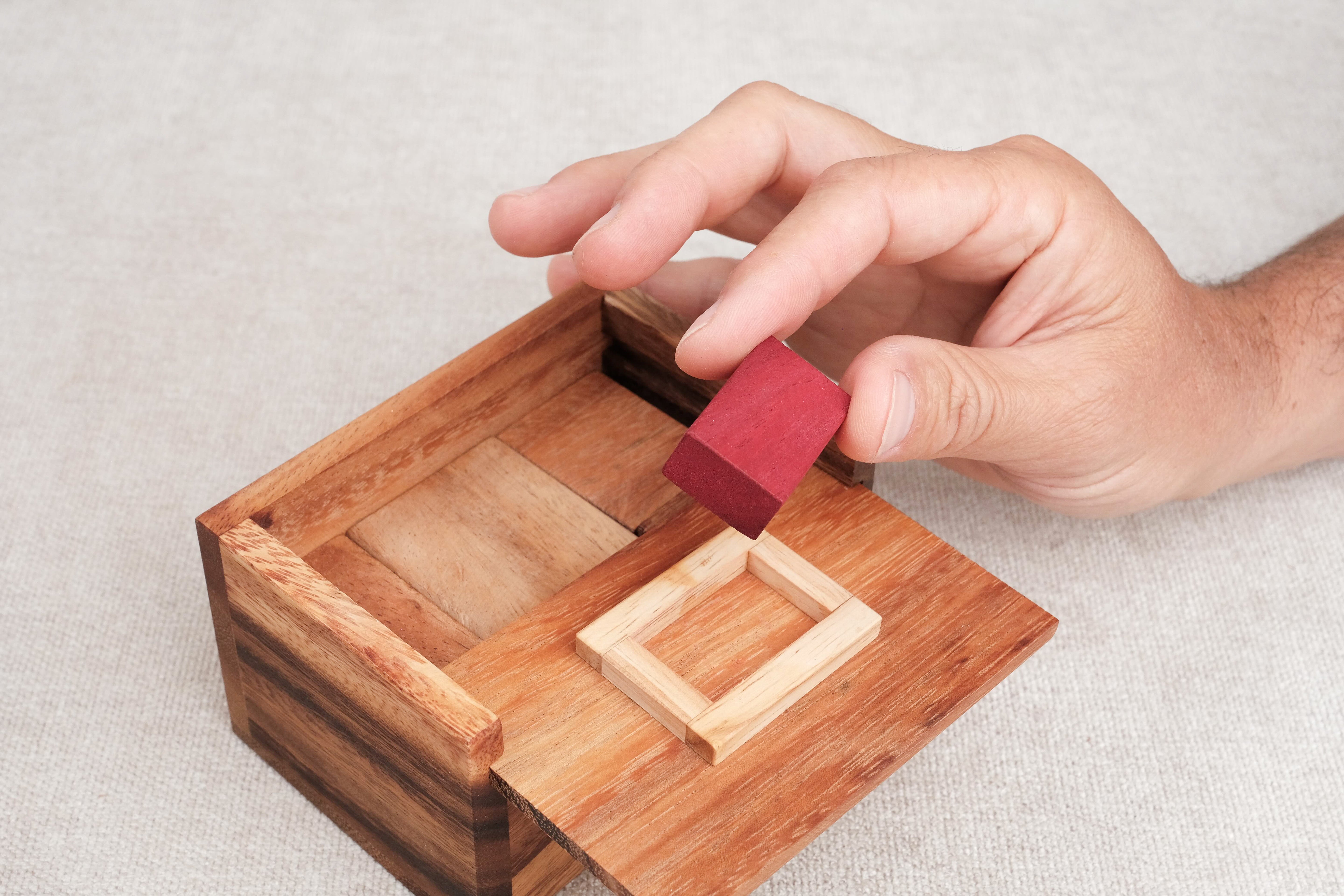 Main insérant la pièce rouge dans la boîte en bois.