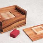 Boîte en bois ouverte avec la pièce rouge et le couvercle posés à côté.