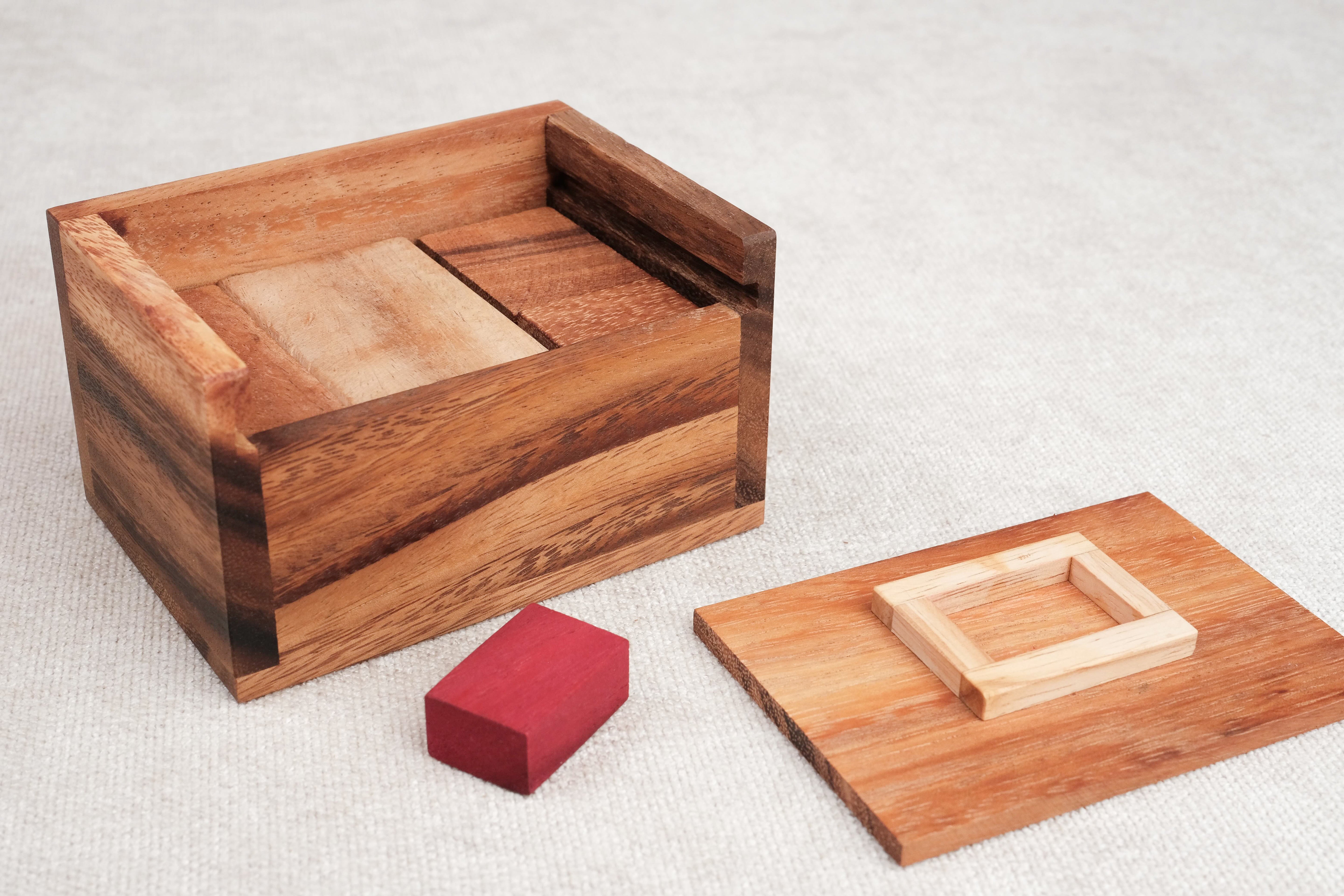 Boîte en bois ouverte avec la pièce rouge et le couvercle posés à côté.