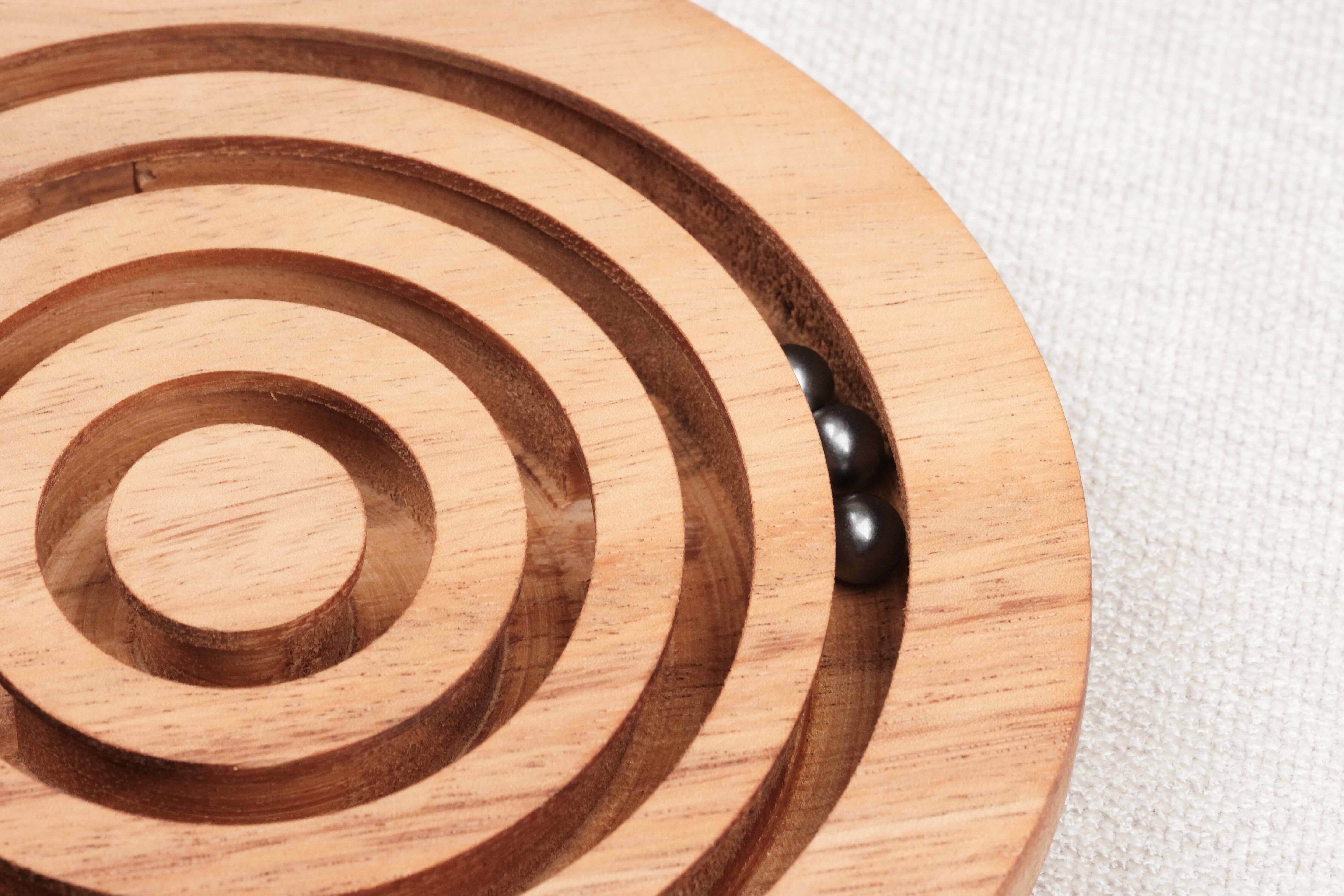 Gros plan sur une bille métallique en mouvement dans les rainures du Labyrinthe en bois – Jeux Faugère