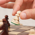 Main déplaçant une pièce d’échecs en bois blanche sur le plateau