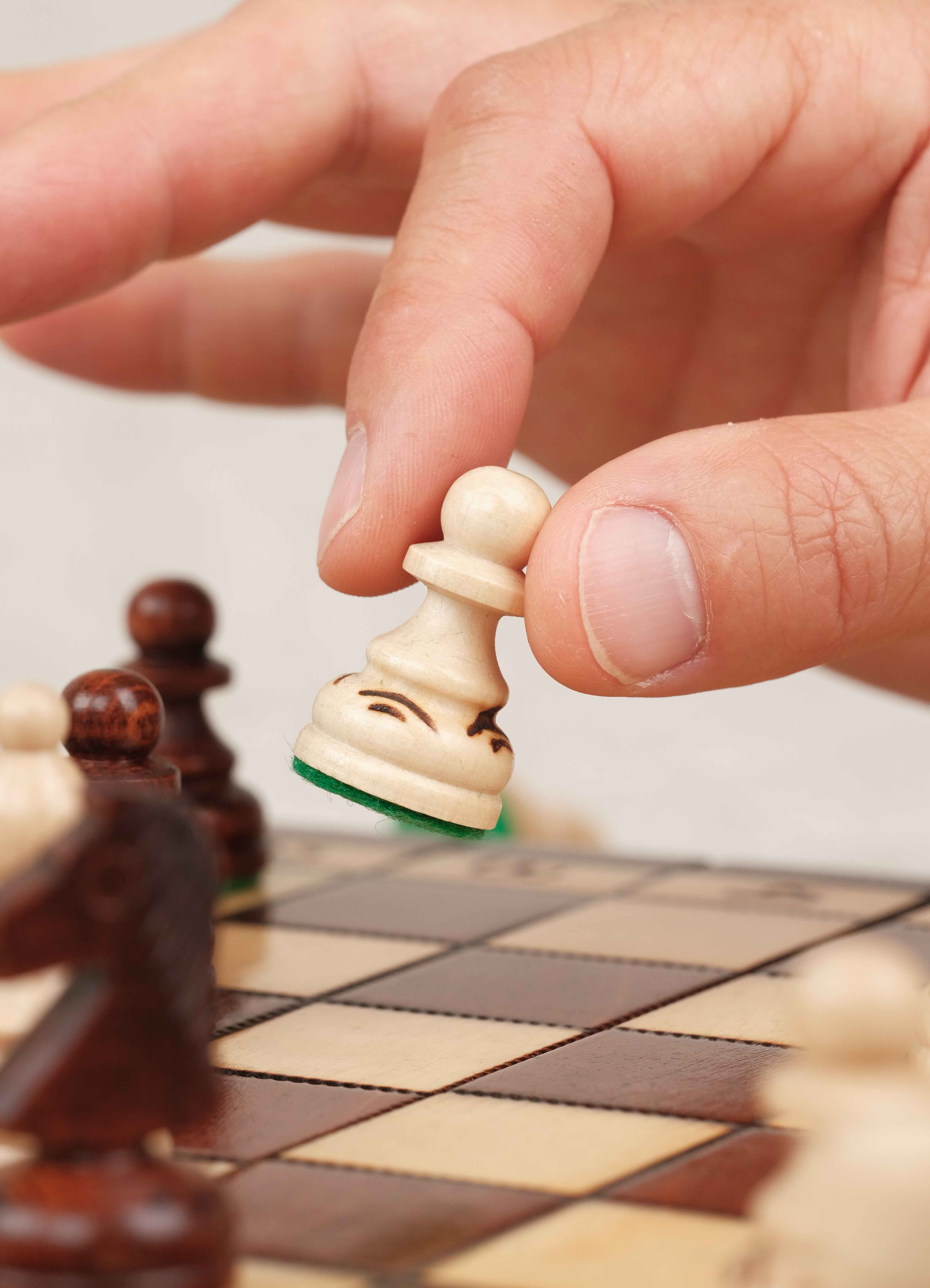 Main déplaçant une pièce d’échecs en bois blanche sur le plateau