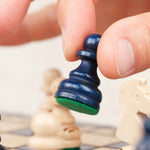 Main jouant une partie sur un plateau d’échecs en bois bleu