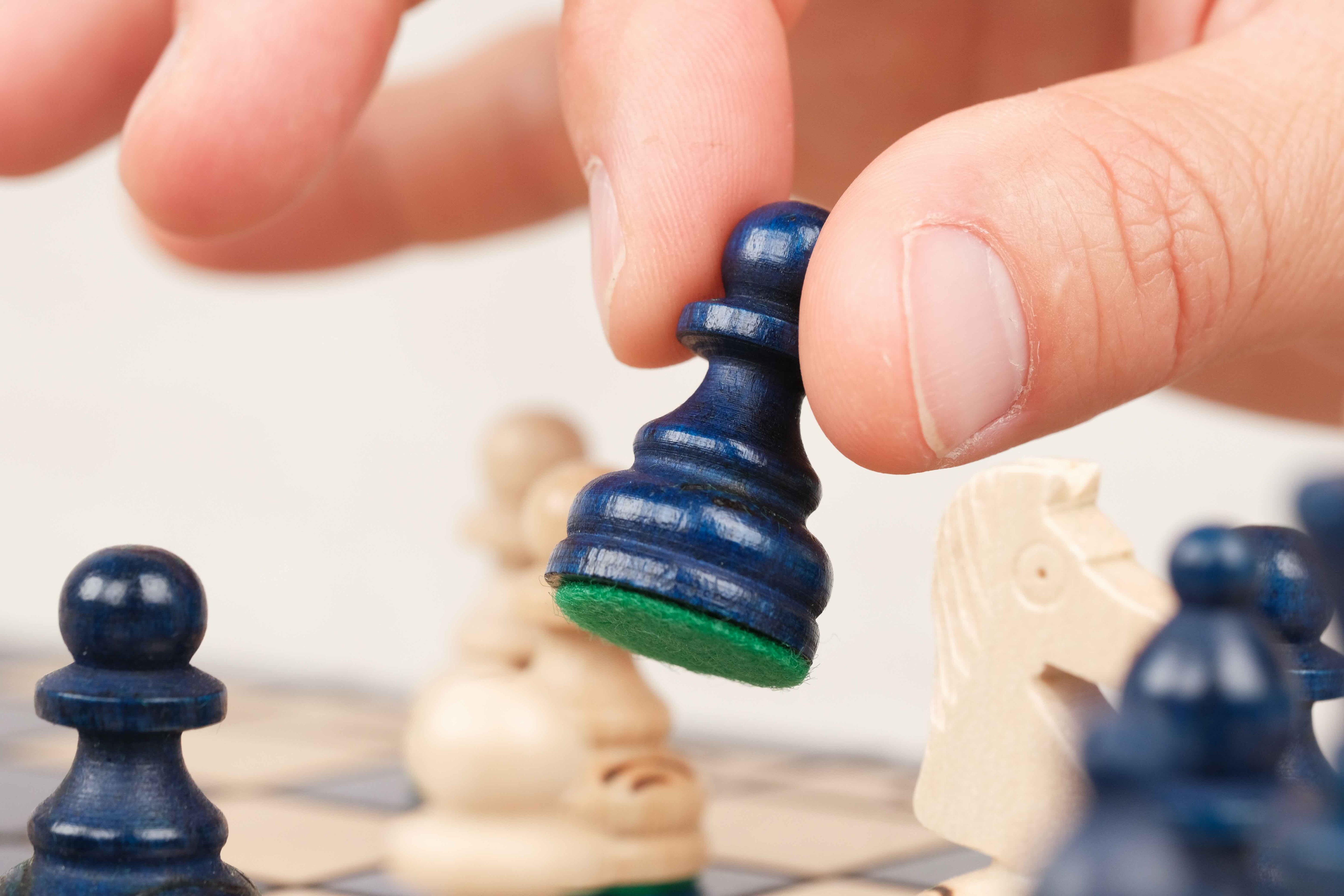 Main jouant une partie sur un plateau d’échecs en bois bleu
