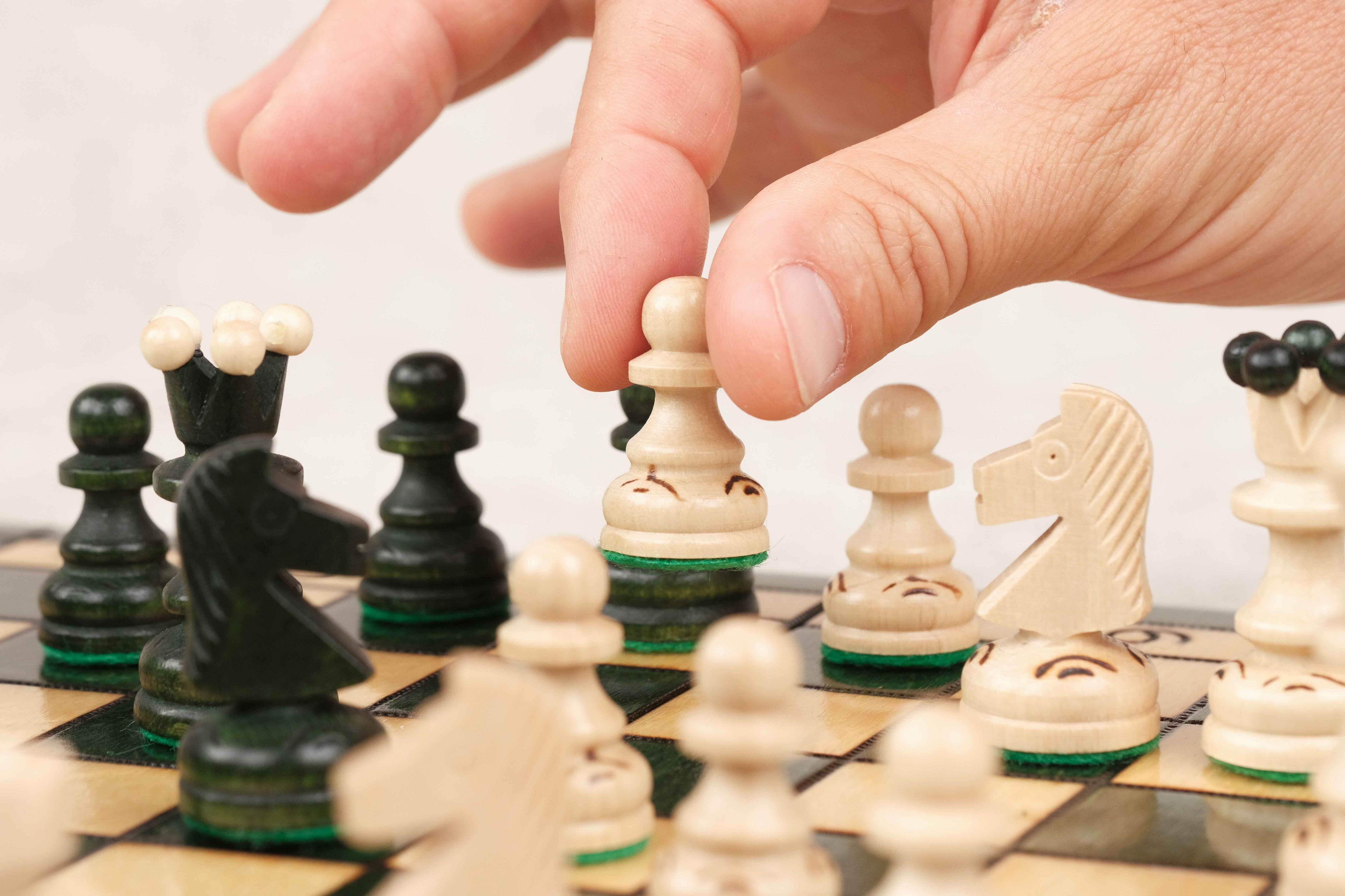 Main jouant une partie sur un plateau d’échecs en bois vert