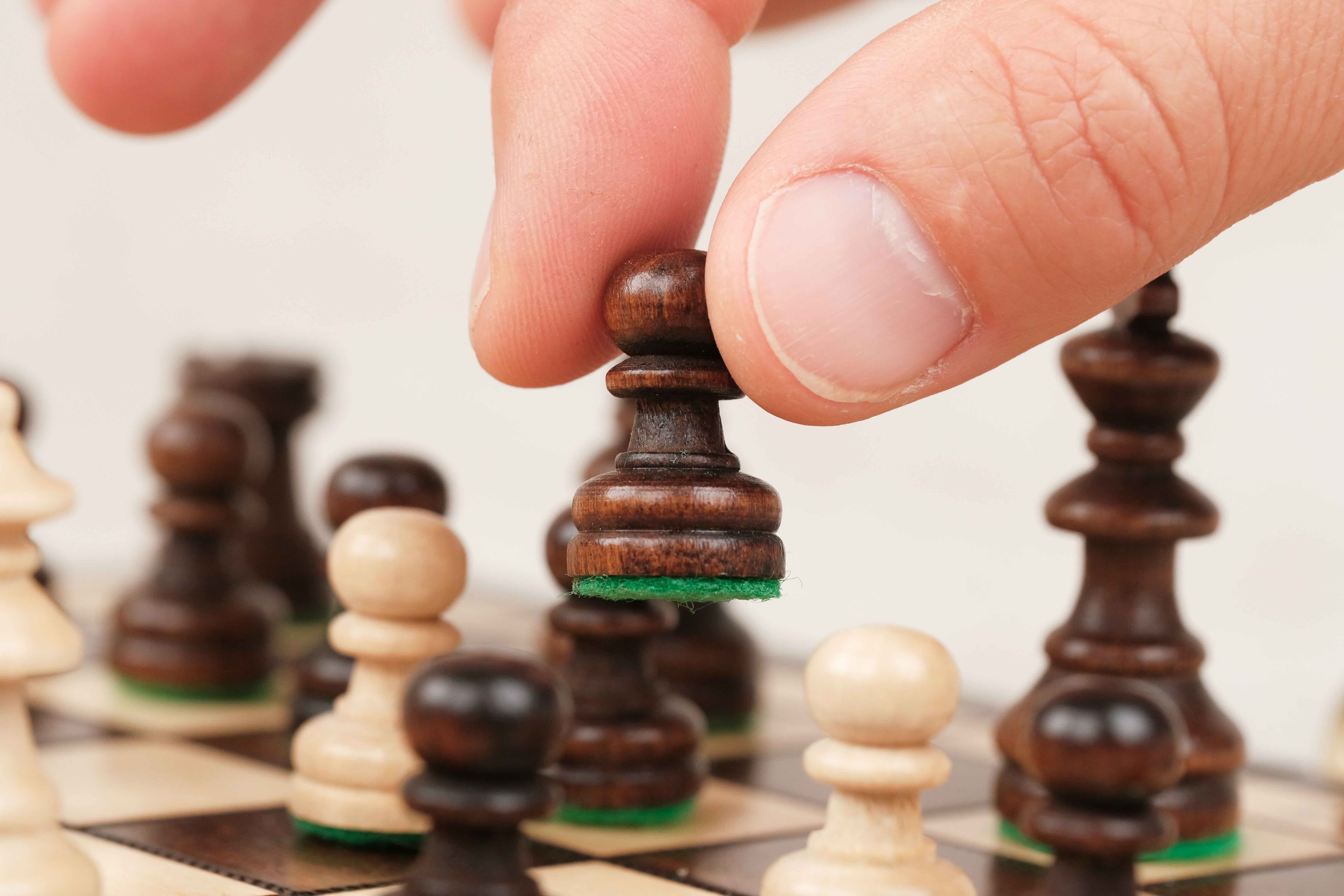Main déplaçant une pièce d’échecs en bois marron sur plateau compact