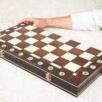 Coffret d’échecs fermé vu de biais, plateau en bois verni avec des mains