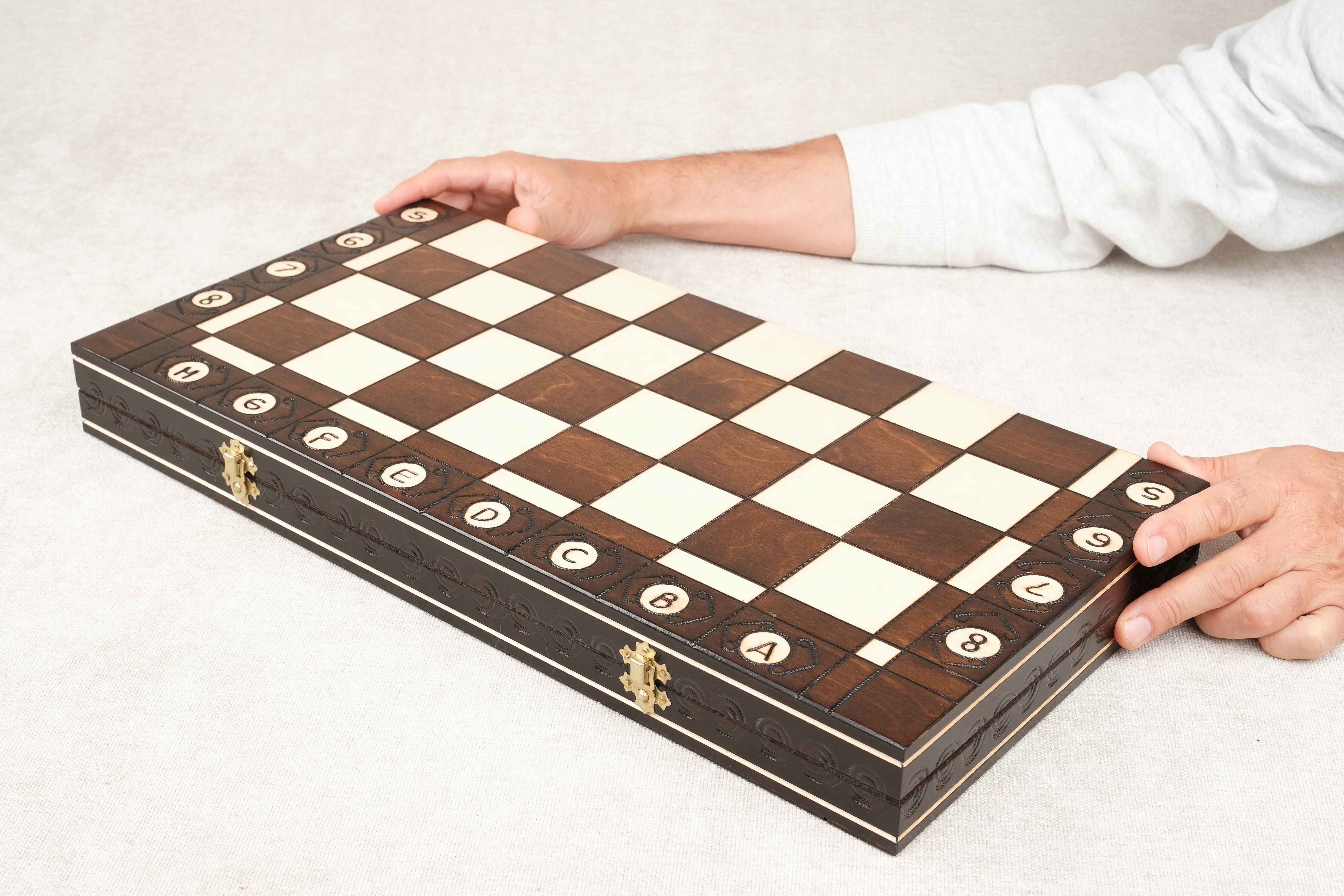 Coffret d’échecs fermé vu de biais, plateau en bois verni avec des mains
