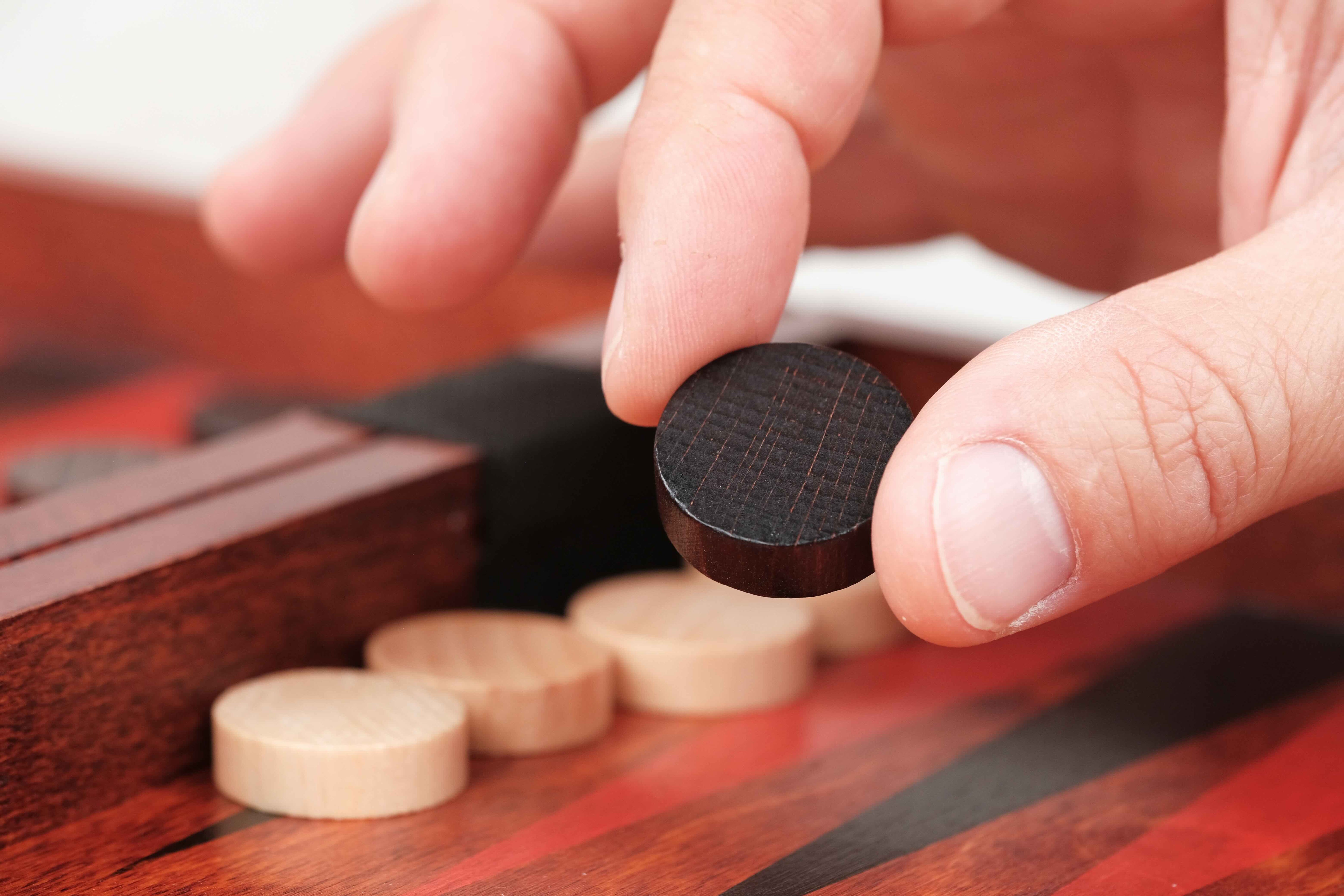 Main déplaçant un pion en bois noir sur le plateau de Backgammon