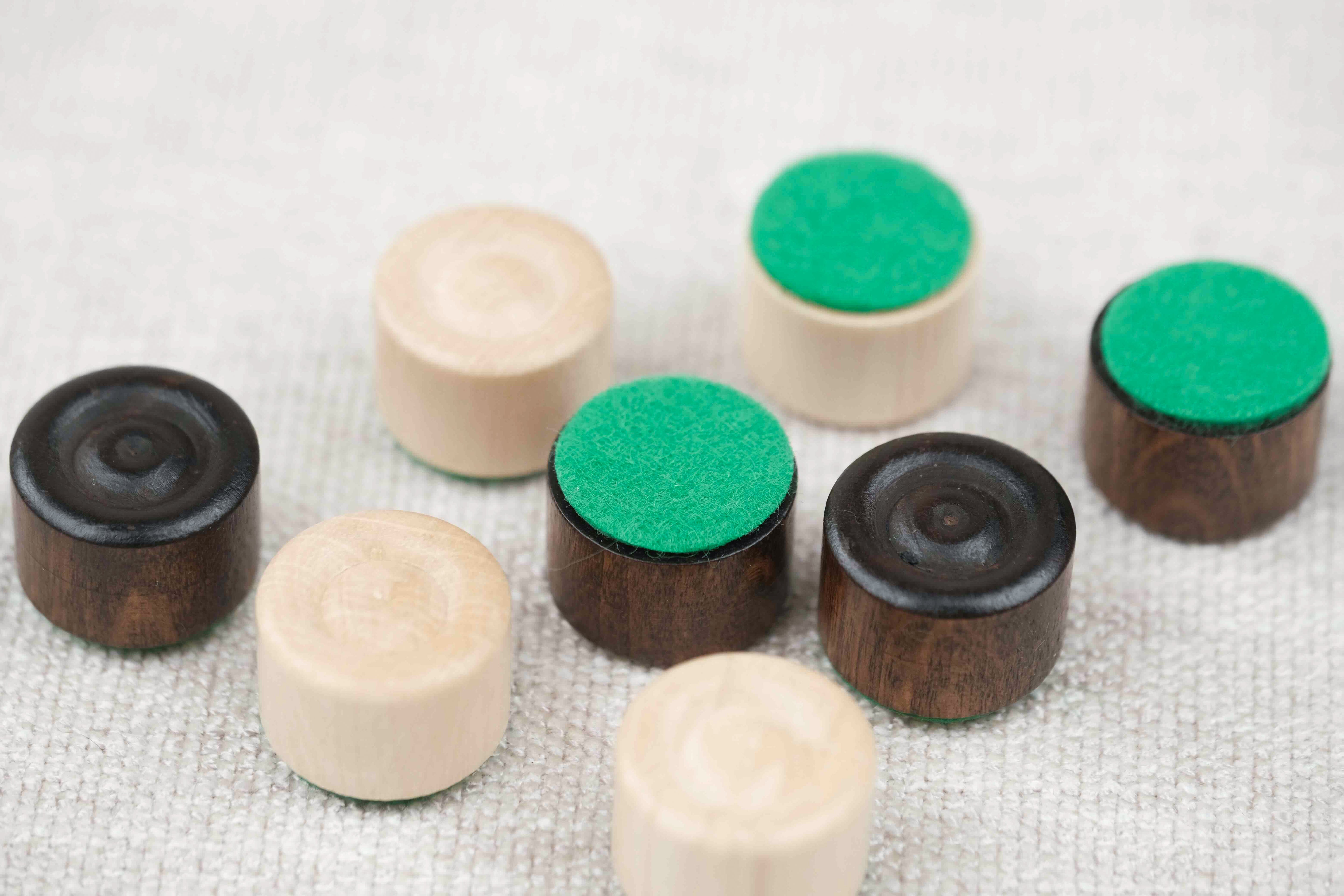Zoom sur les pions de dames en bois clair et foncé et bases feutrine
