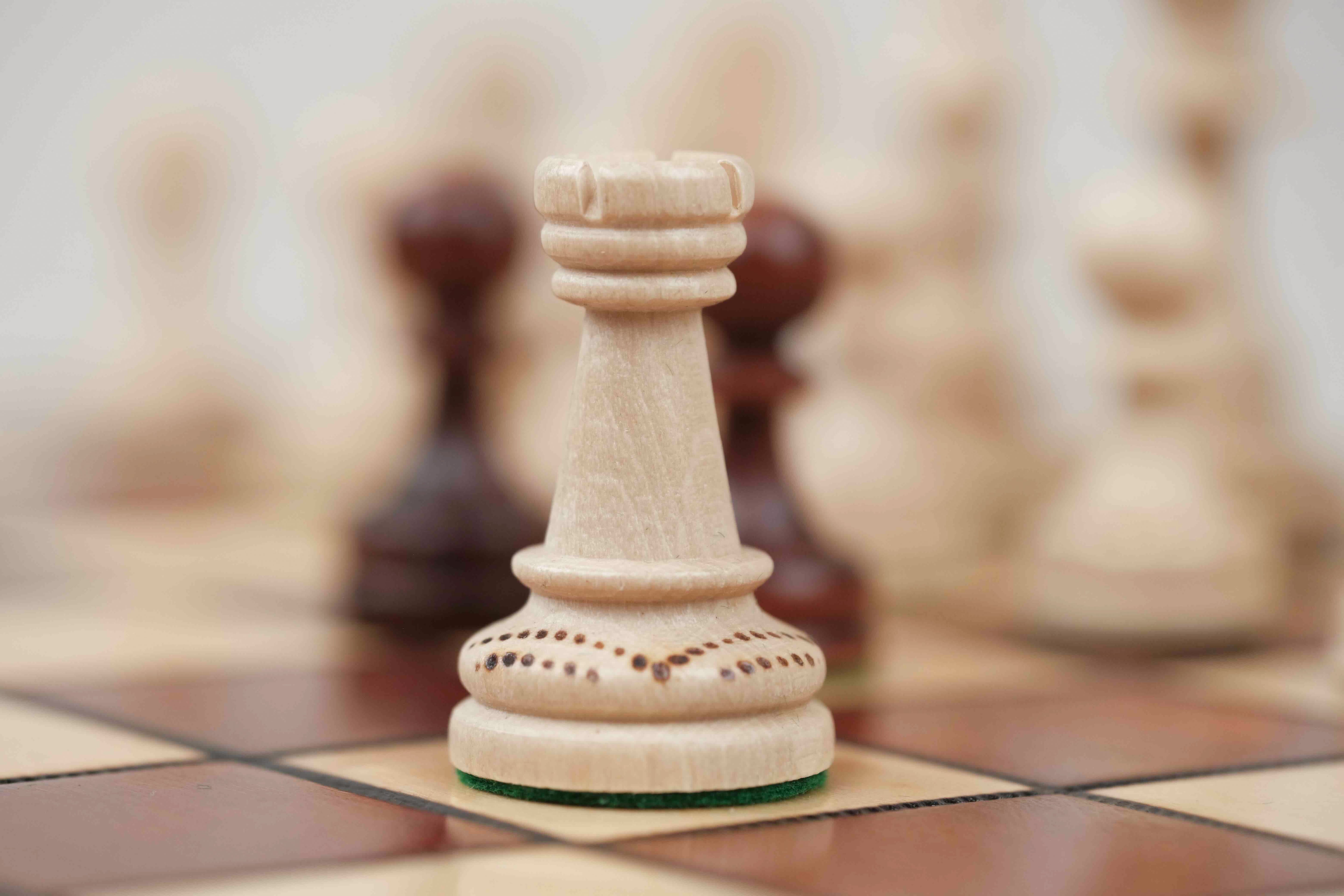 Pièce d’échecs blanche en bois avec détails sculptés sur plateau marron clair