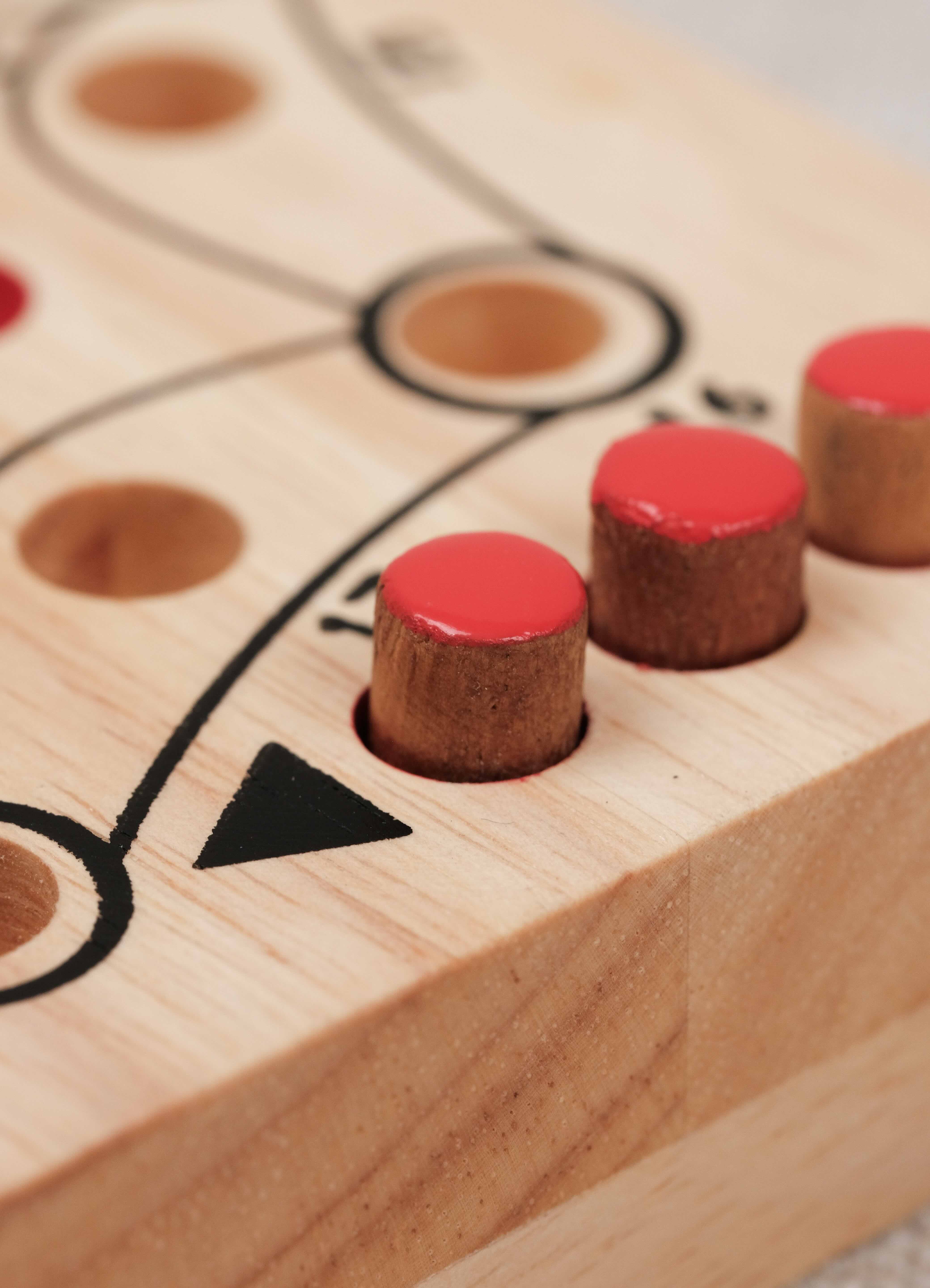 Détails des pions rouge en acacia placés dans les trous gravés du plateau Jeu de tock (toc) L clair en hévea