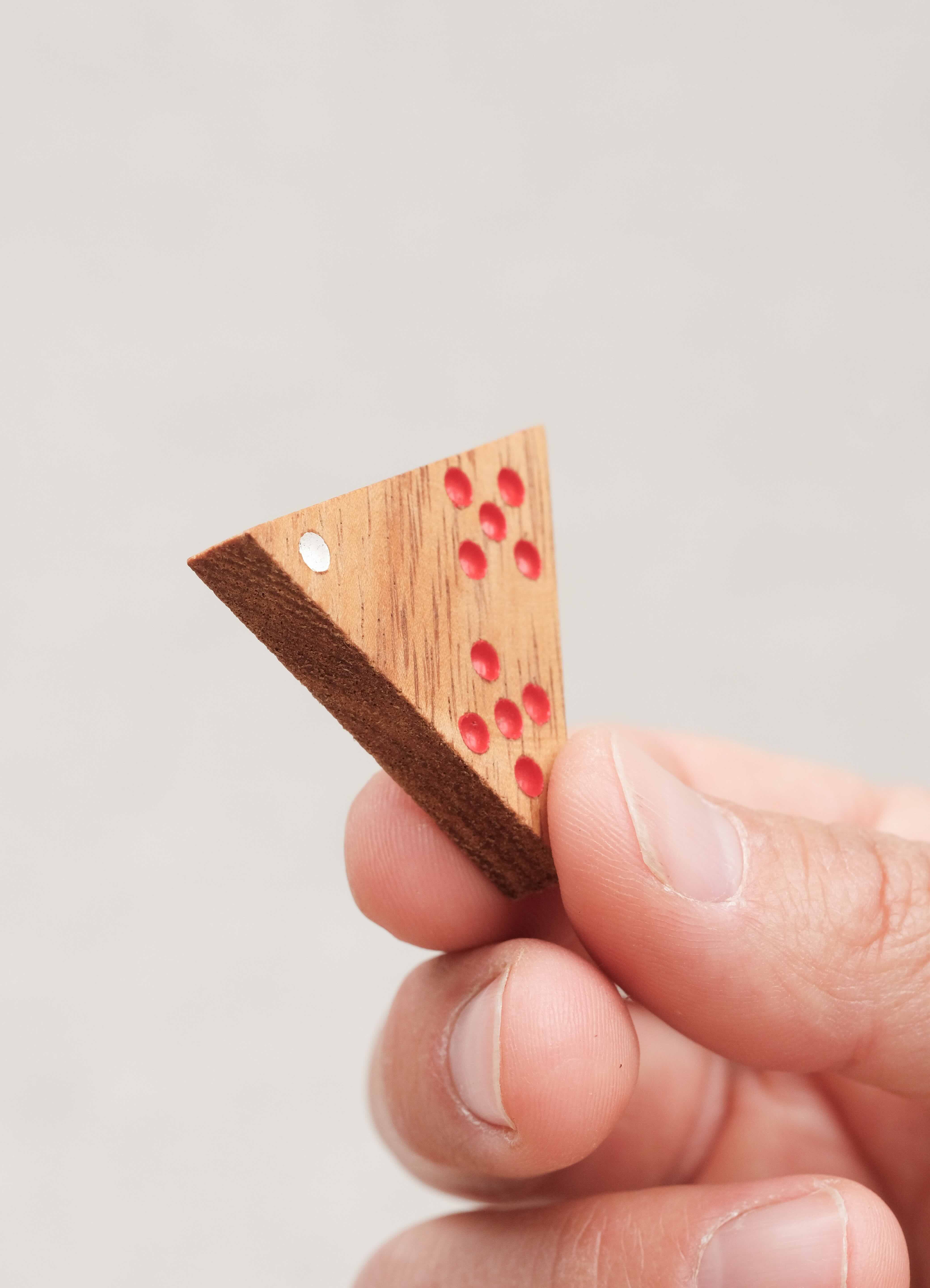 Pièce triangulaire gravée et colorée de Triomino tenue en main