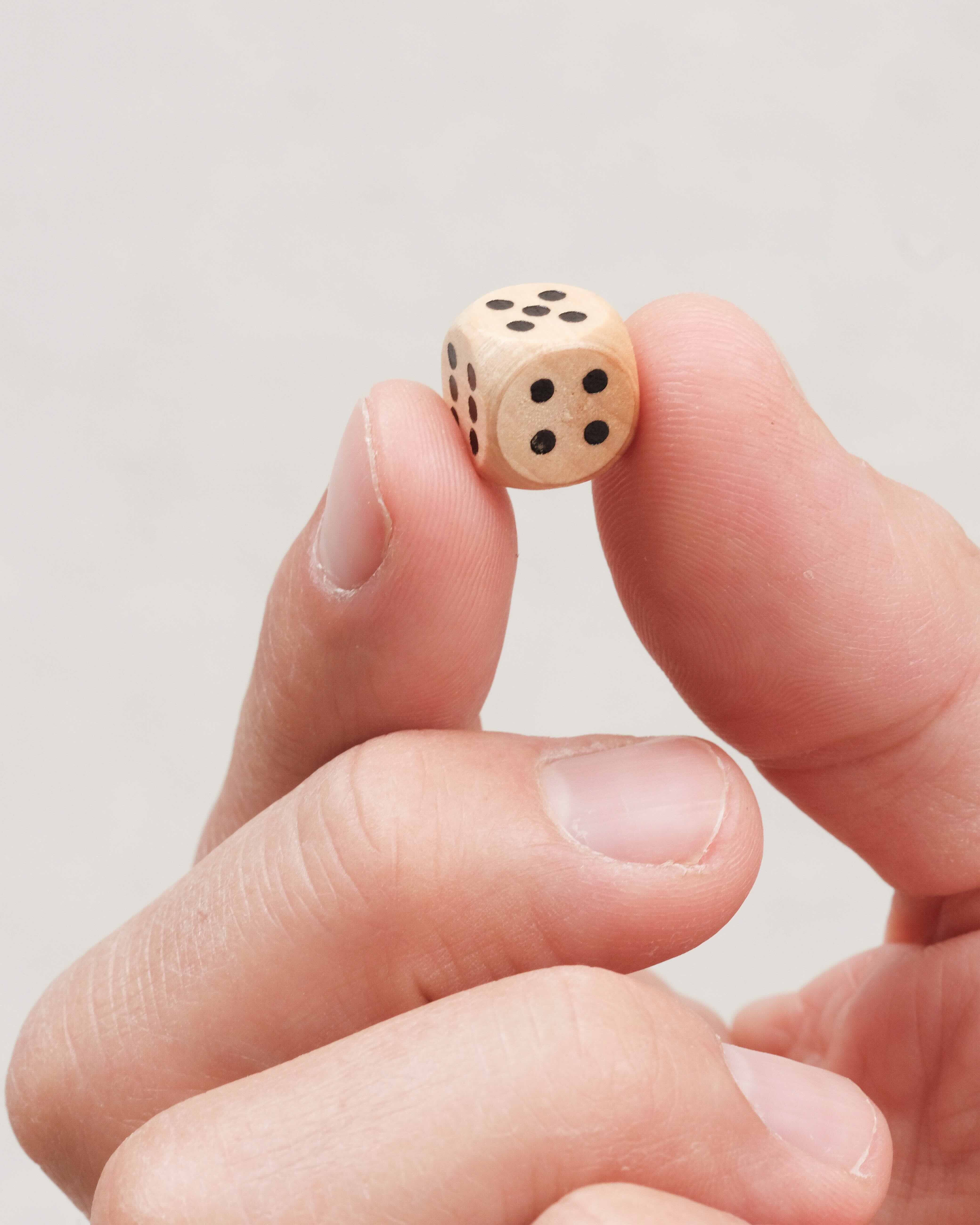 Main tenant un dé en bois du jeu Ferme la Boîte petit modèle.
