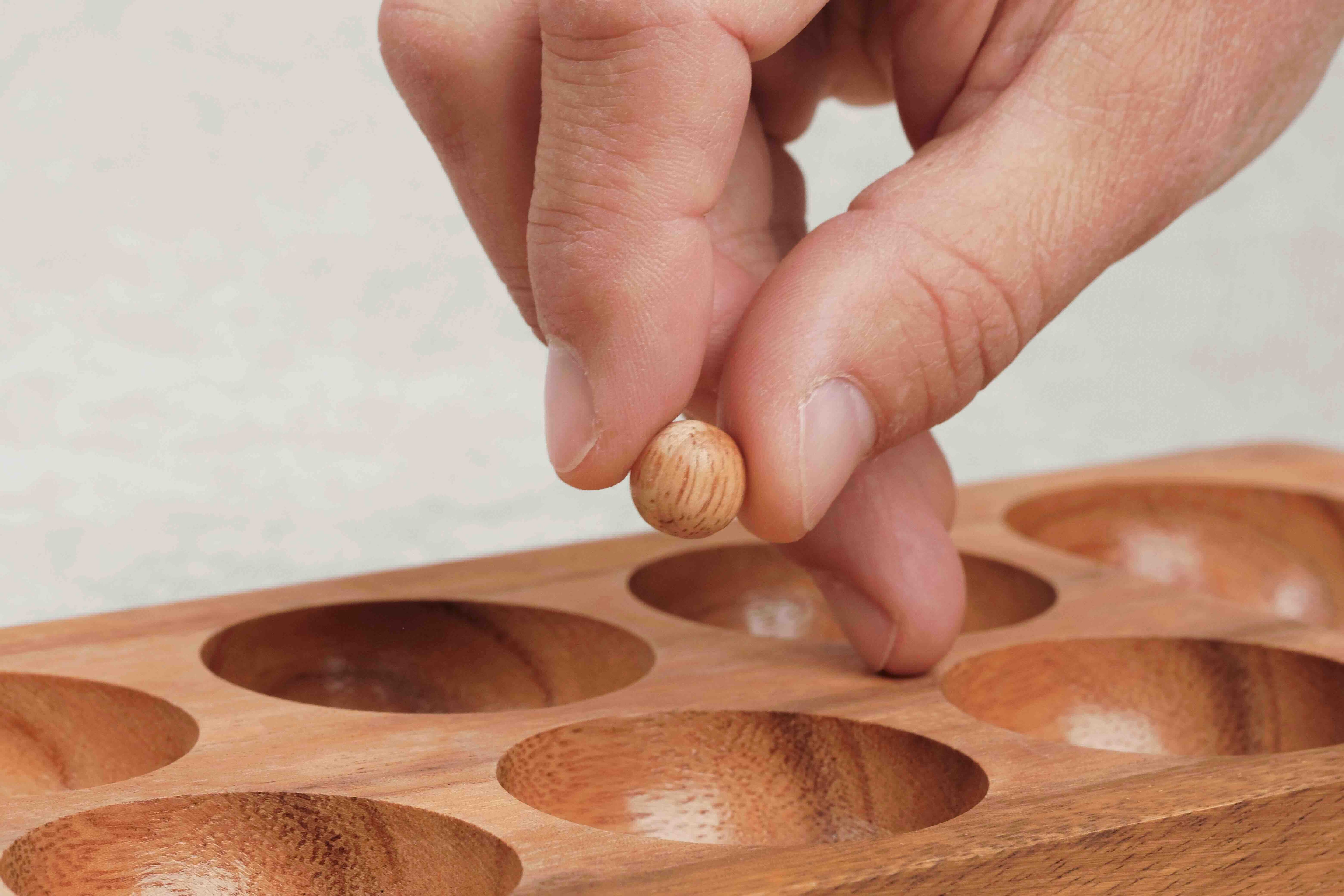 Main plaçant une bille dans une alvéole du Kalaha