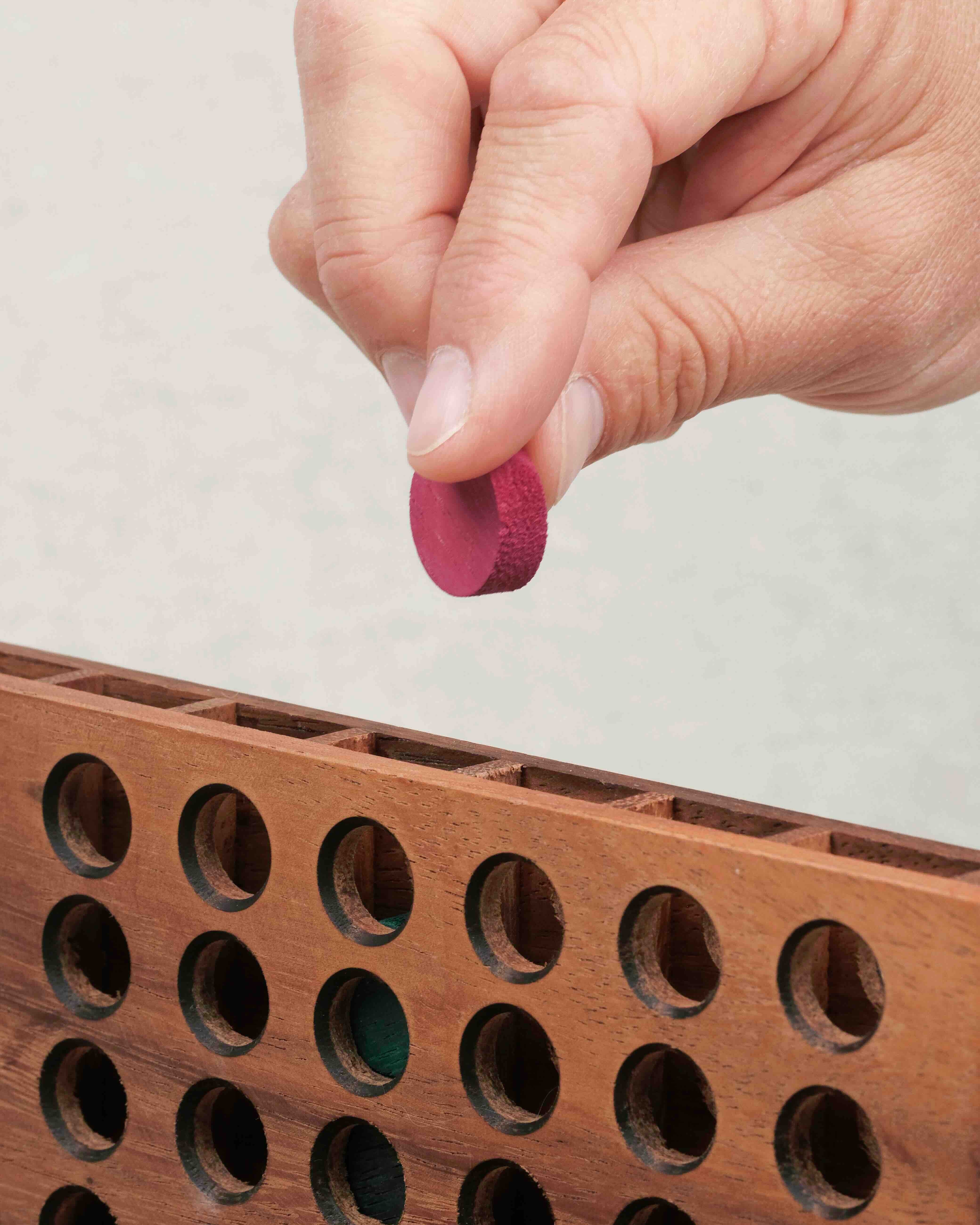 Main plaçant un jeton dans la grille du Puissance 4 en bois
