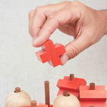 Main plaçant une pièce croix rouge sur la structure en bois