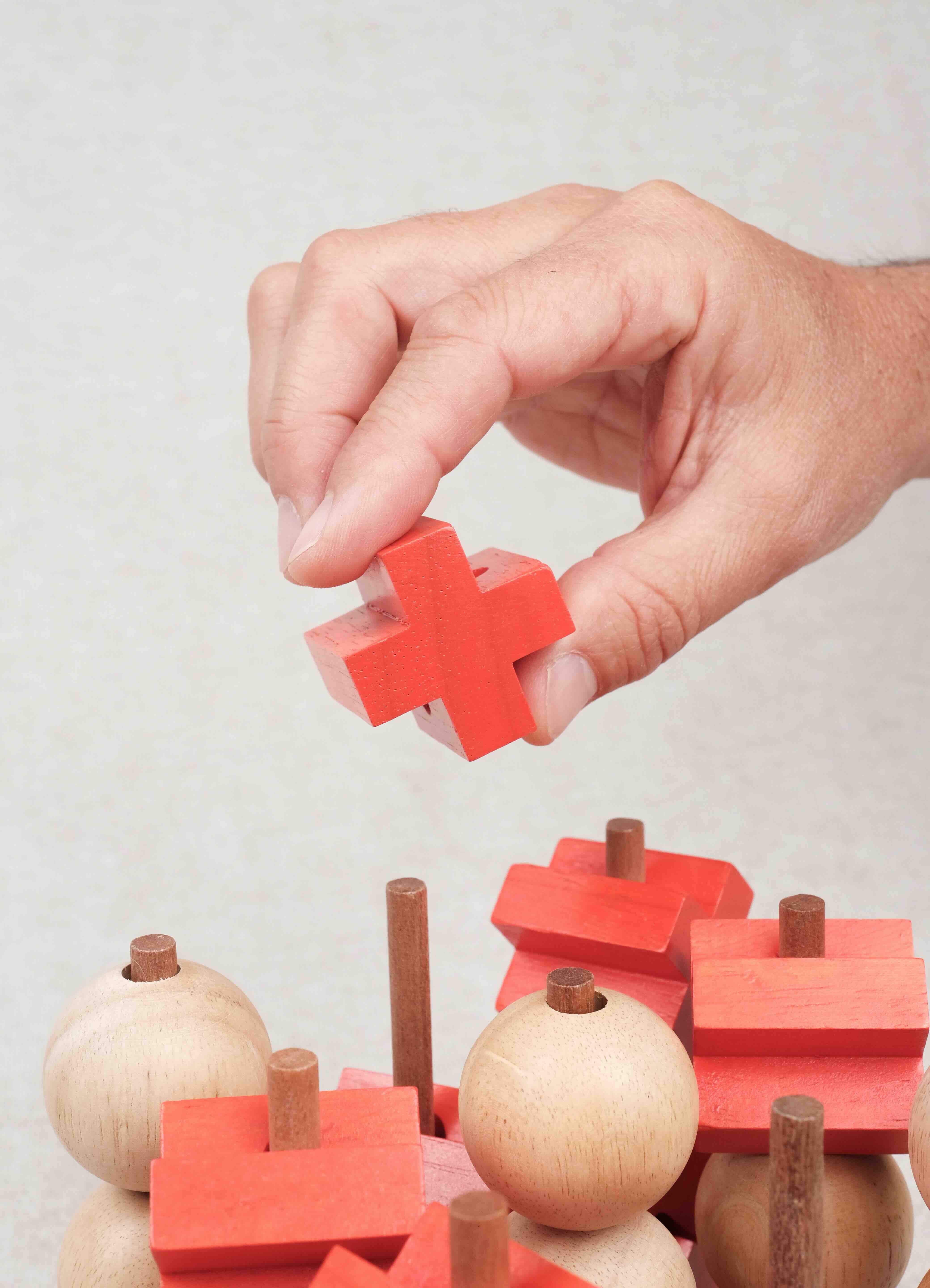 Main plaçant une pièce croix rouge sur la structure en bois