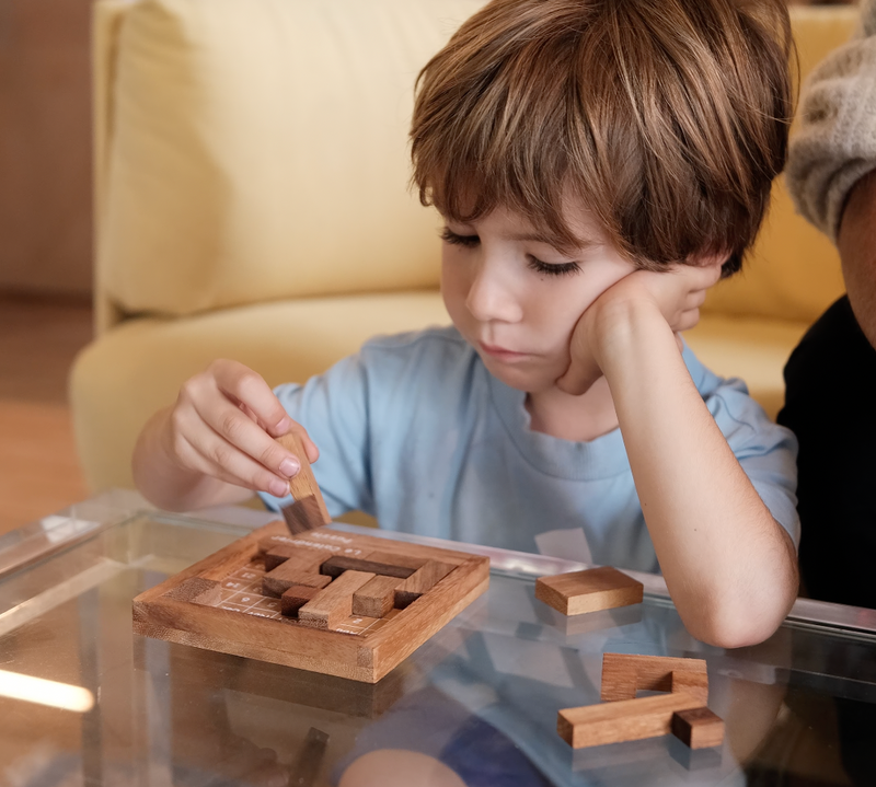 Garçon concentré sur un casse-tête en bois posé sur une table basse