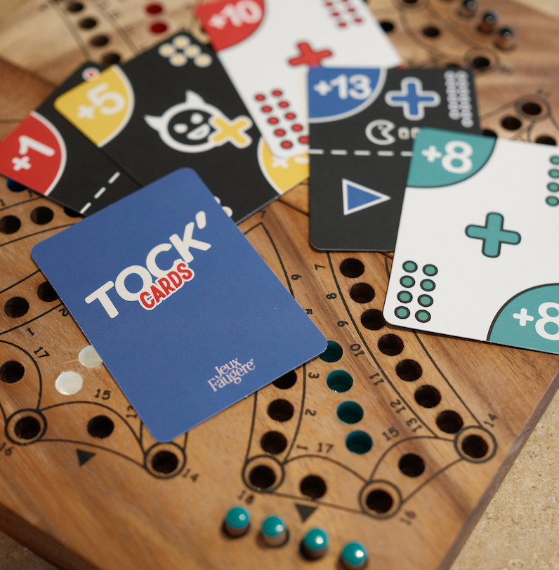 Cartes Tock'CARDS illustrées étalées sur un plateau de jeu de Tock en bois avec ses pions