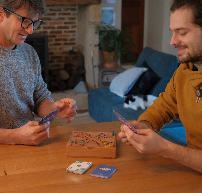 Deux hommes jouent à un jeu en bois avec des cartes autour d'une table
