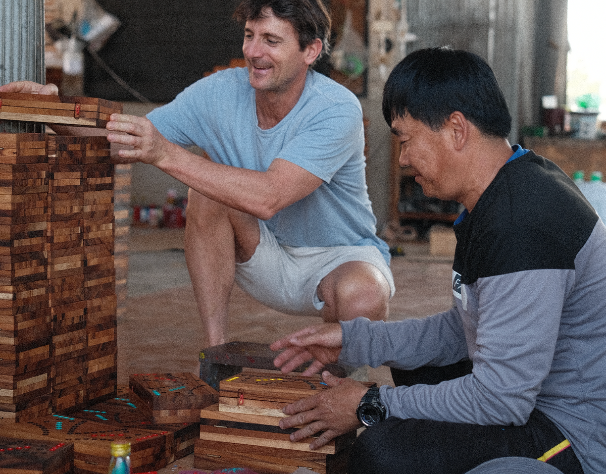 Deux hommes accroupis devant des empilements de pièces de jeux en bois dans l'atelier