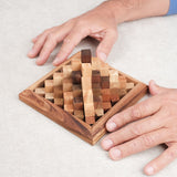 Deux mains reconstituant le casse-tête Grande Kheops en bois sur une table.