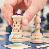 Main déplaçant une pièce sur le plateau d'échecs bleu grand format en bois Jeux Faugère