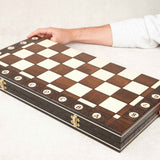 Coffret d’échecs fermé vu de biais, plateau en bois verni avec des mains