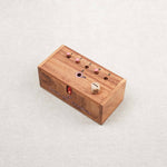 Coffret du jeu "Le trou du cochon" avec dé en bois et pions roses sur le dessus