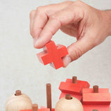 Main plaçant une pièce croix rouge sur la structure en bois